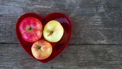 Fresh sweet apples in red heart shaped vase on wooden background.