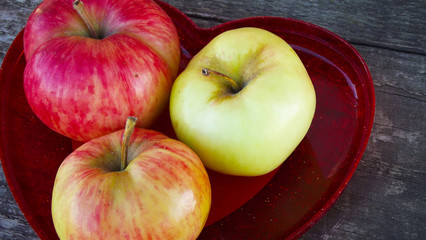 Fresh sweet apples in red heart shaped vase on wooden background.