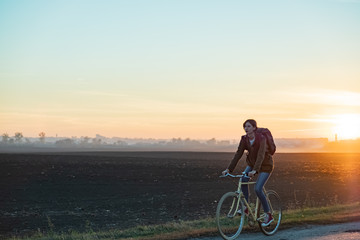 Fototapeta na wymiar Female commuter riding a bike out of town in rural area. Young woman riding bike at sunset