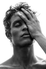 Portrait of a young, fit man with black hair and strong features with hand covering half of face, in black and white