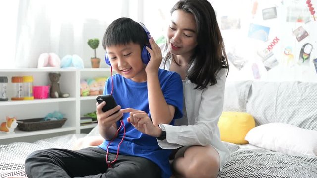 Mother and son wearing headphones using smartphone for listen to music together at home