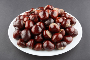 Many chestnuts on white plate. Grey background
