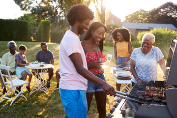Couple grilling at a black multi generation family barbecue - obrazy, fototapety, plakaty