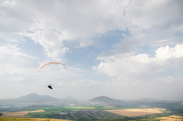 A white-orange paraglider flies over the mountainous terrain
