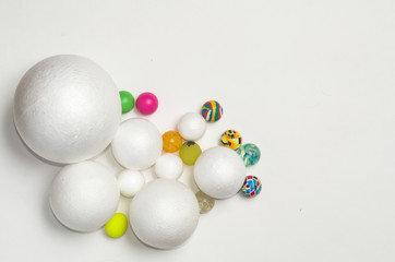 Eight white balls of plastic, different sizes and ten balls of the same size and different colors lie on a plane, on a flat background, in a dense composition, copy space.