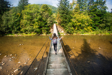 Tourist woman walk by long wooden suspension bridge above river. balance concept