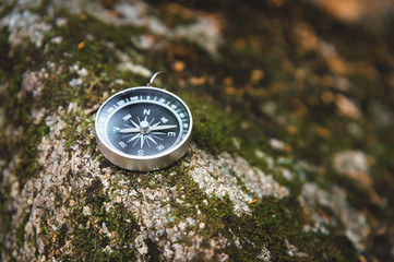 Magnetic compass with a black dial on a wild stone covered with green moss. The concept of finding...