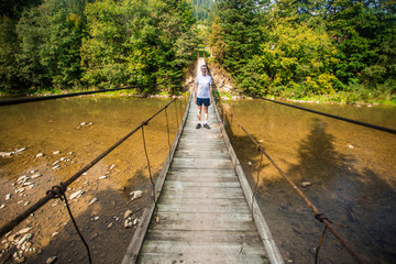 Tourist man walk by long wooden suspension bridge above river. balance concept