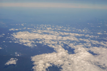 The sky and clouds and the view seen in the window of the plane.
