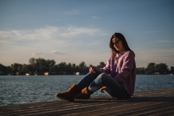 Fototapeta na wymiar Lonely girl with glasses sitting by the river in sunset