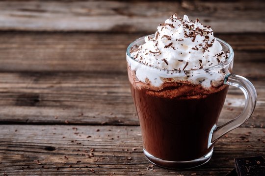 Hot chocolate drink with whipped cream in a glass on a wooden background