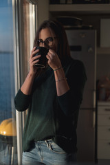 Girl with glasses drinking coffee by the kitchen window