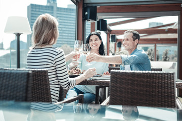 Best friends. Handsome man keeping smile on his face while sitting in semi position and touching bocals with his friends