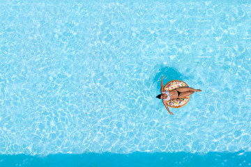 Woman on a donut buoy in a blue water swimming pool aerial view from above - obrazy, fototapety, plakaty
