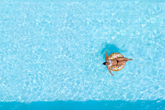 Woman on a donut buoy in a blue water swimming pool aerial view from above