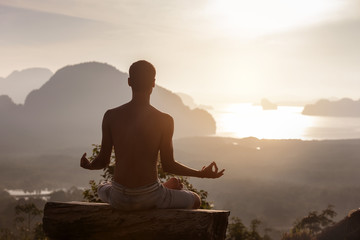Man sits in yoga pose at sunrise against sea