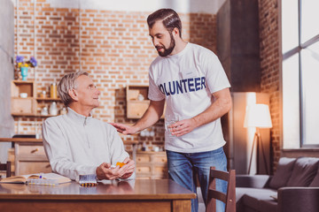 Kindness. Bearded smiling man holding a glass of water and the man taking some pills