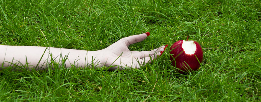 una mano estirada de mujer con tez blanca sobre c&eacute;sped verde con una manzana mordida 