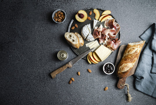 Cheese and ham plate with parmesan, camamber, goat cheese, ham, baguette and snacks. Overhead view, dark background