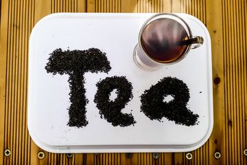 Top View closeup of Hot cup of tea with written word tea by tea leaf on a brown wooden table