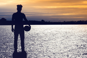 Amazing silhouette of football soccer player boy standing and holding a ball  on the beach in sunset time