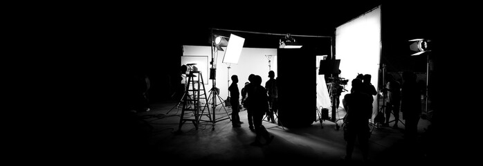 Silhouette images of video production behind the scenes or b-roll or making of TV commercial movie that film crew team lightman and cameraman working together with director in big studio - obrazy, fototapety, plakaty