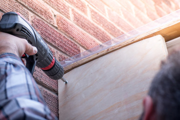 Closeup of Man Using a Power Drill building a house porch at home in a sunny day