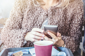 girls holding a red paper Cup with coffee and and typing a message on your smartphone. Means of communication