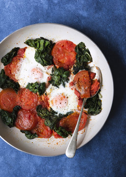 Cooked tomatoes, eggs and silverbeet in a pan with a spoon.