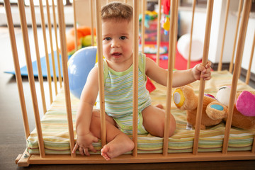 Cute smiling baby looking through the wooden bars of his crib or playpen with a happy smile indoors...