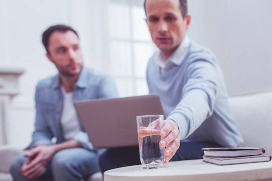 Feeling thirsty. Selective focus of glass with fresh water being taken by professional psychologist for satisfying his clients thirst