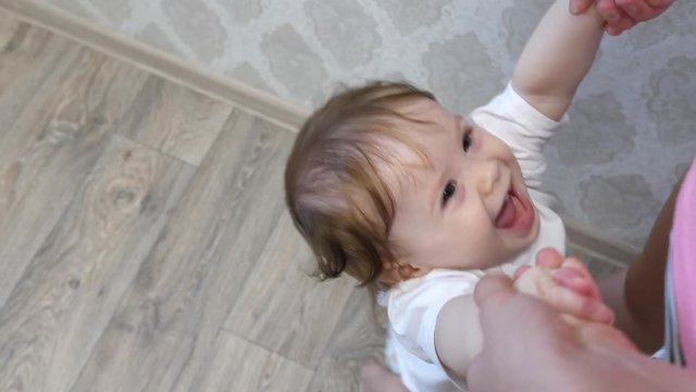 baby plays with mom, holding hands, jumping and laughing in nursery.