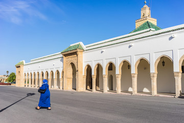 Obraz premium Woman walking by the small mosque in the mechouar. Located at a large parade ground attached to the Dar-al-Makhzen which is the primary and official residence of the king of Morocco in Rabat.