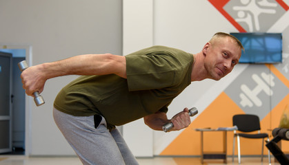 Fototapeta premium A man goes in for sports, exercises with dumbbells in the gym.