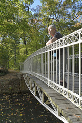 seniorin steht im herbstlichen schlosspark worms-herrnsheim auf einer br&uuml;cke