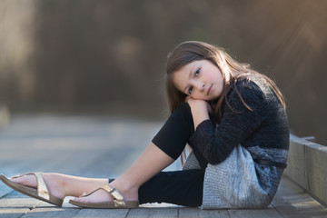 Young girl with long brown hair and a sweater dress posing on a wooden pathway