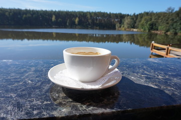 A porcelain cup of coffee that sits on the side of the balcony, with a magical view of the lake.