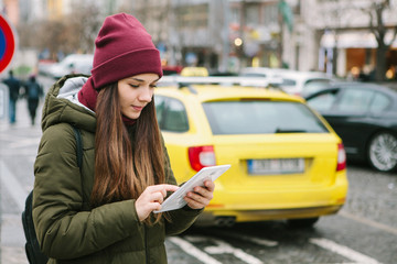 Beautiful tourist girl with a tablet on a street in Prague calls a taxi or looks at a map or uses the Internet or a mobile application. Travel or tourism.