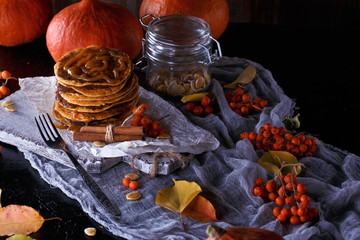 Autumn concept. Pumpkin pancakes with caramel topping, with pumpkins, leaves on a dark background.