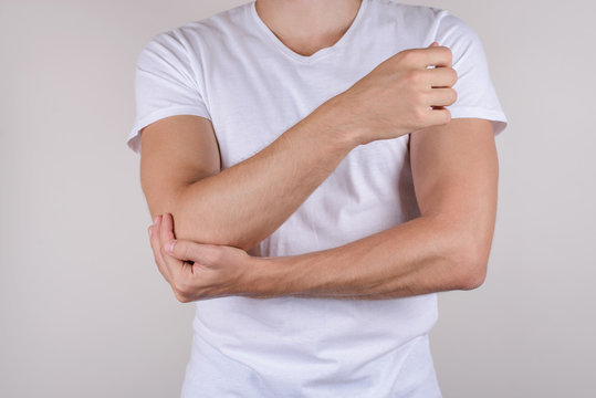 Cropped close up photo portrait of unhappy upset sad guy holding touching painful elbow wearing white t-shirt isolated grey background copy space
