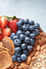 Fresh ripe fruits, blueberry, almond nuts, oat flakes, crisps on a plate on a gray background.