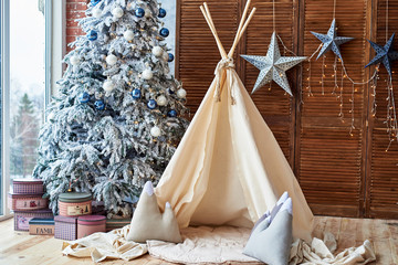 Christmas tree with gifts and wigwam near window in child room, copy space. Christmas decorations. Childen room interior with decorated play tipi tent. Scandinavian style © mirage_studio