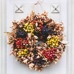 Wreath of dried berries and leaves on wooden door of house.