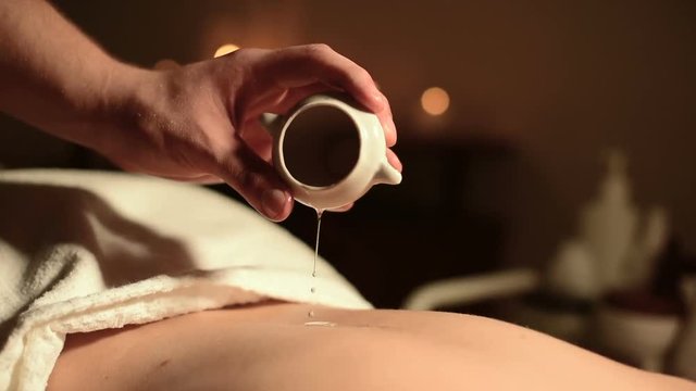 Close-up of male hands in a rescued salon before a massage. Massage oil in a dark room on the background of burning candles is poured onto the girl's skin