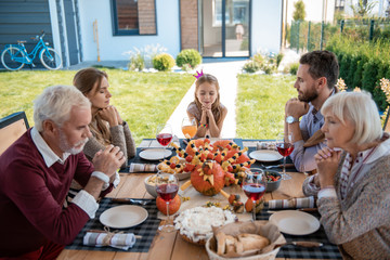 Vegetarian family. Concentrated people sitting at the table while keeping eyes closed