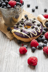 Baked donuts with dried blueberries and a chocolate on the wooden rural table. The doughnut with fresh blueberries and raspberry.
