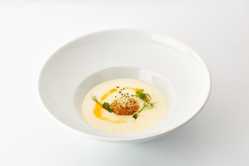 cream soup with greens in a large white plate isolated on white background