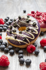 Baked donuts with dried blueberries and a chocolate on the wooden rural table. The doughnut with fresh blueberries and raspberry.