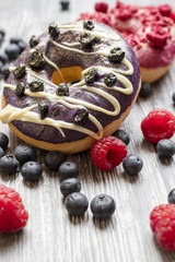 Baked donuts with dried blueberries and a chocolate on the wooden rural table. The doughnut with fresh blueberries and raspberry.