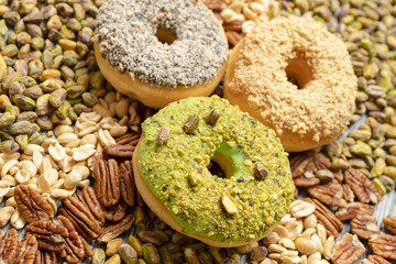 Set of three American doughnuts on pecan nuts, pistachios and peanuts. Candy shop concept. 